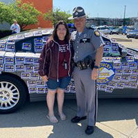 Madison County Special Olympics athlete with Kentucky State Trooper in front of a cruiser at the 2022 Cover the Cruiser stop in Richmond.