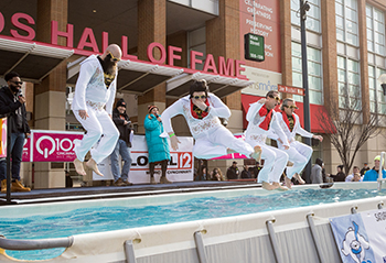 Four Polar Plunge participants in white Elvis Presley jumpsuits about to hit the water in various Elvis poses.