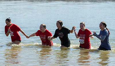 Five women hold hands as they walk back out of the lake at the 2023 Western Kentucky Polar Plunge.