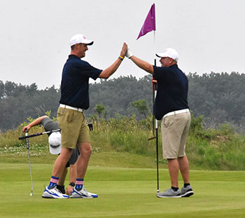 Golfers Wake Mullins and Dennis Gaines give each other a high five on the green in front of a flag.