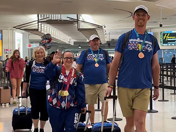 Special Olympics Kentucky coach and athletes walk into the reception area at Louisville Airport towing their carry-on bags.