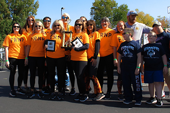 A group of women in orange shirts hold their trophies while they are joined by Special Olympics athletes who stand on the right side of the photo.