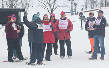 A group of smiling volunteers greets snowshoers as they finish their race at the State Winter Games