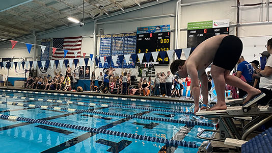 A swimmer sets in his starting block about to dive in front of a large crowd.