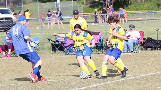 Three soccer players battle for the ball.