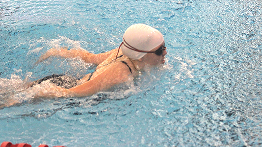 A swimmer in a swim cap starts to pull her arms out of the water for a butterfly stroke.