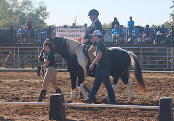 Rider on horse passing State Equestrian Competition sign.