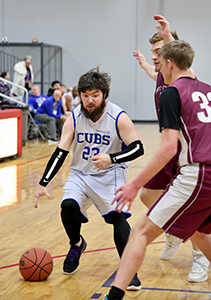 Basketball player in a white uniform dribbling against a defender in a Maroon uniform.