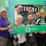 Several people pose with a Team Kentucky photo frame in front of them.