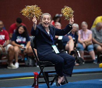 Tonya Cornett waving gold pom pons at the 2022 USA Games gymnastics competition.