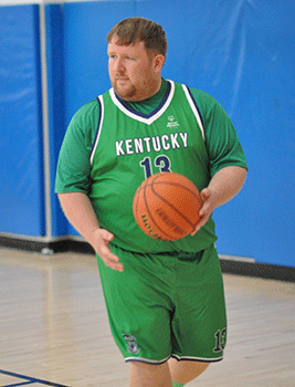 A man in a green basketball uniform dribbling the ball. 