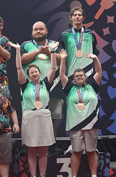 Four bowlers on medal stand. Two in front are waving.