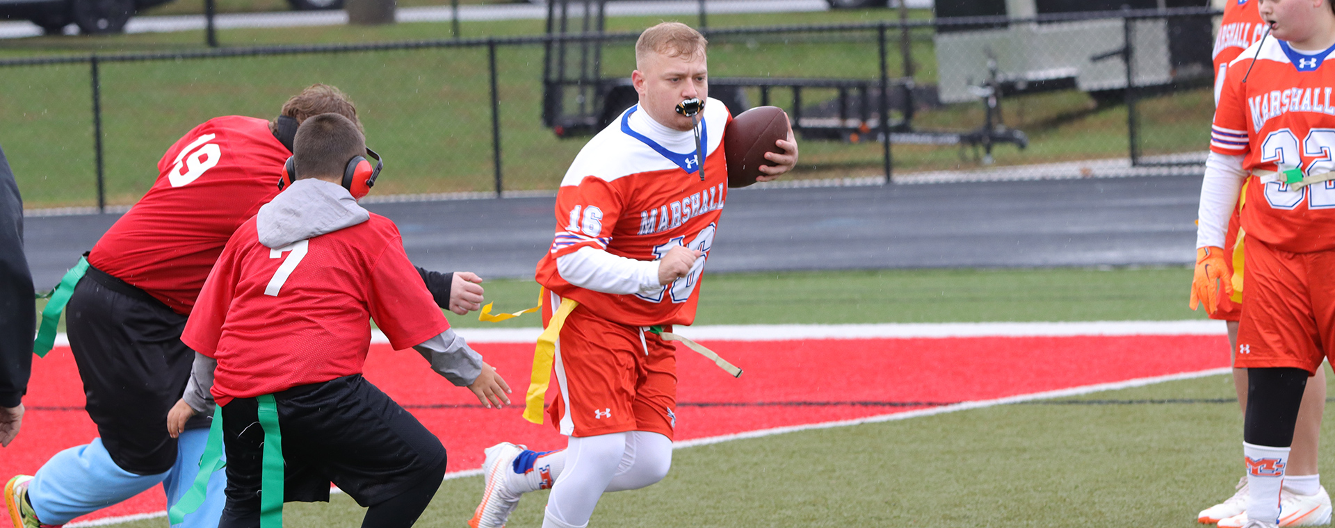 Flag football player with the ball running from defenders.
