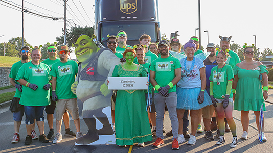 People dressed as Shrek characters in front of an 18-wheeler.