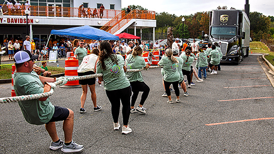 People pulling a truck with a rope in front of a large crowd.