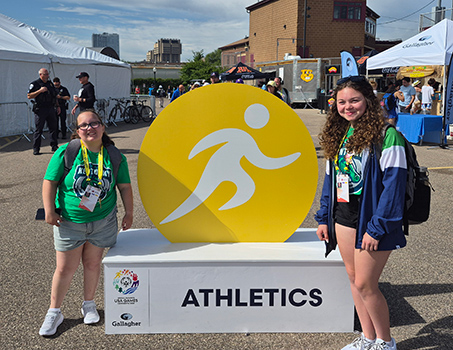 Olivia Pruitt and Maya Hetler next to the Athletics venue sign.