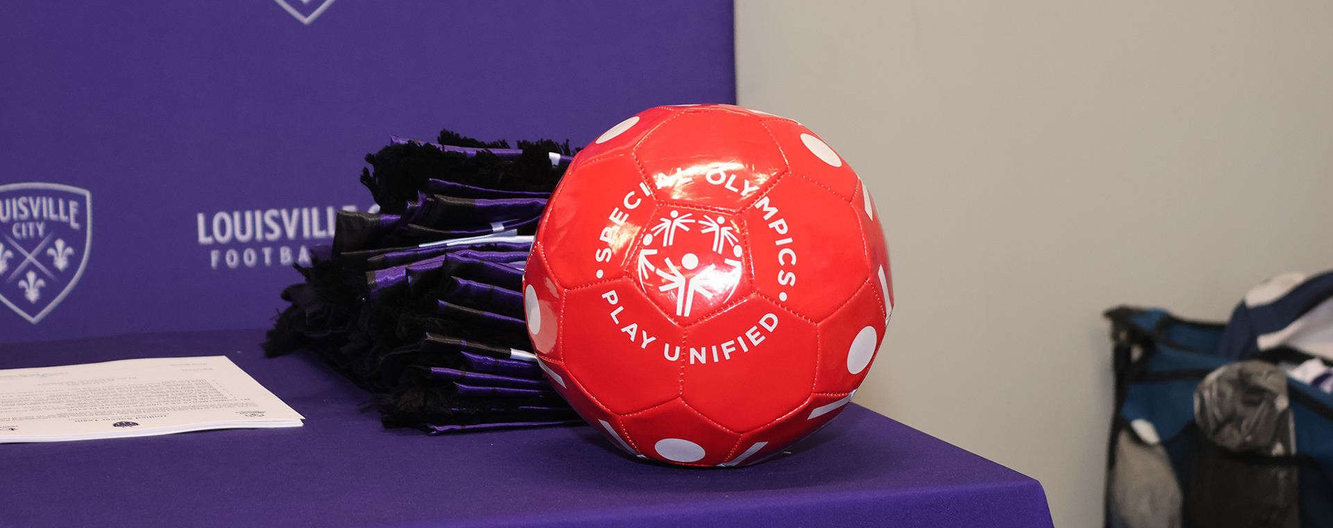 Red soccer ball with a Unified sports logo on a table with a purple tablecloth.